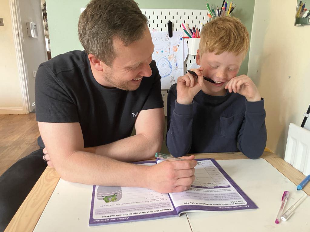Ieuan tutoring a child — laughing together over a maths workbook during a home visit